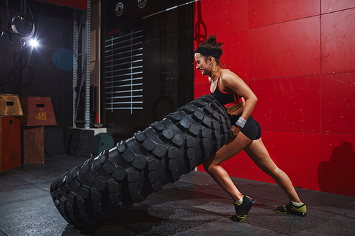 Active and strong woman flipping tyre with help of arms and knee