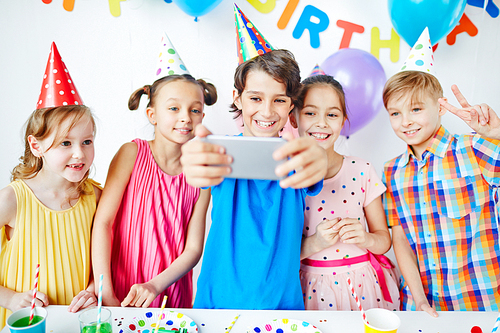 Cute boy with cellphone making selfie at birthday party