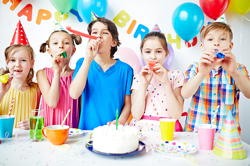 Row of happy kids blowing horns at birthday party