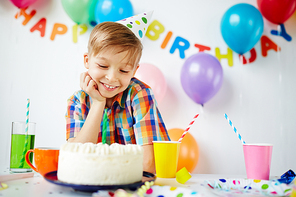 Happy boy sitting at the table and looking at birthday cake