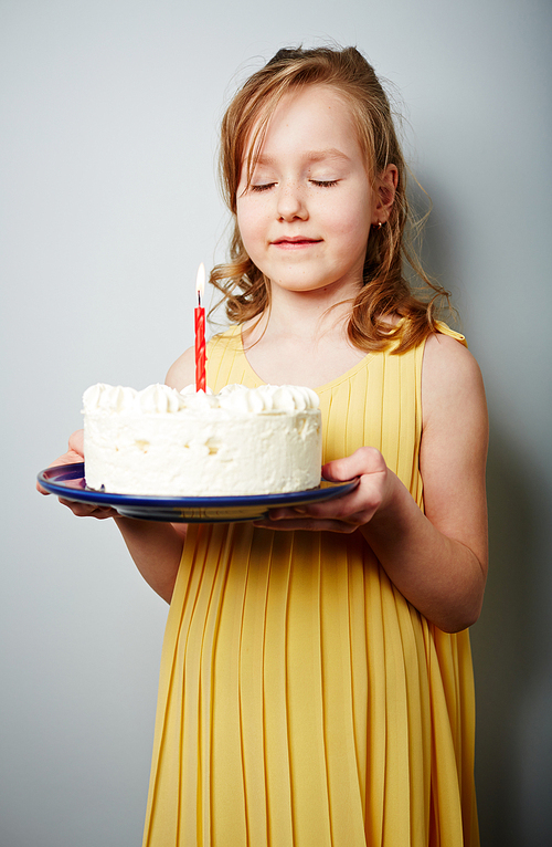 Cute girl holding birthday cake with burning candle and making wish