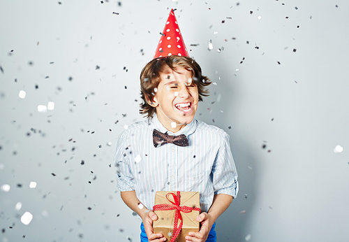 Ecstatic boy in birthday cap holding packed gift