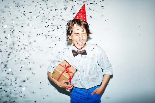 Ecstatic boy with packed birthday gift standing in confetti fall