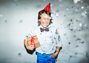 Excited boy with gift standing under confetti