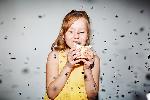Little girl eating cake under confetti rain