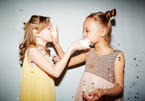 Two little girls giving a piece of cake to each other