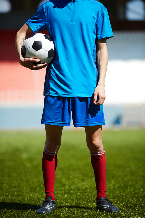 Young footballer with soccer ball standing on the field
