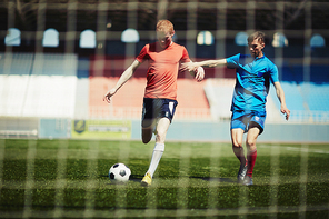 Football player going to shoot the goal, his opponent trying to prevent it