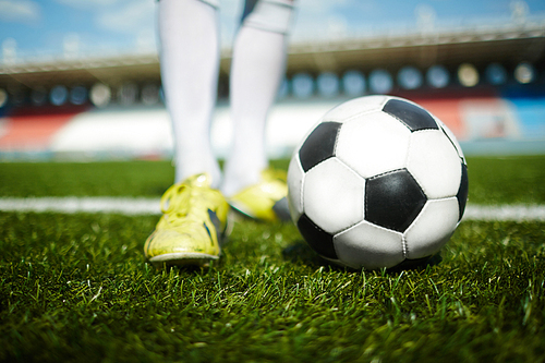 Close-up of soccer ball on field and athlete standing near by