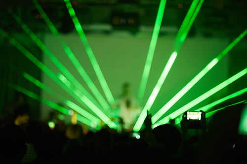 Defocused image of crowd enjoying performance and musician on stage in bright green rays of strobe lights