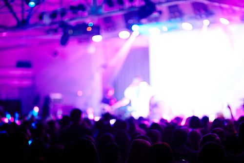 Blurred image of performer on purple-lit stage before large crowd of fans admiring his music