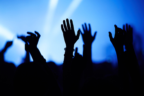 Silhouettes of people at concert with hands raised
