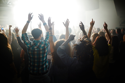 Crowd of ecstatic fans with raised hands dancing by songs of their favorite modern singer at live concert