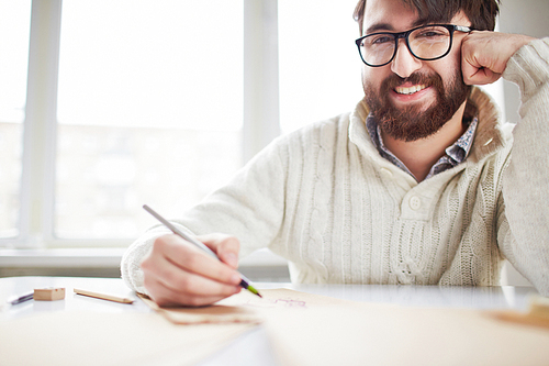 Portrait of smiling artist in glasses sitting at the table and drawing