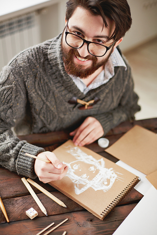 Smiling man in glasses drawing a picture at the table