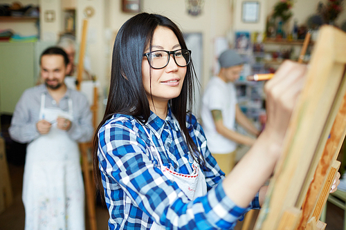 Asian student in eyeglasses drawing on easel