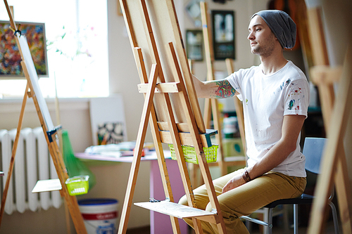 Young student sitting by easel and drawing