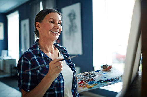 Happy elderly woman looking at her painting in art studio