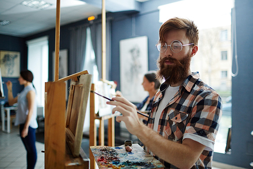 Skilled guy with palette painting something on easel