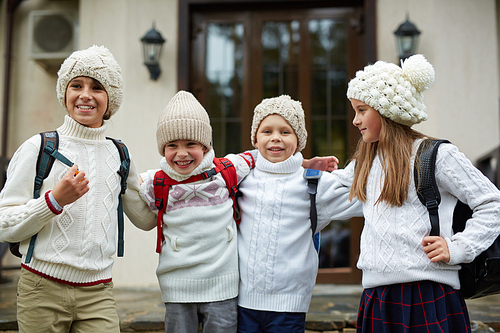 Carefree kids in knitted casual-wear standing by their school