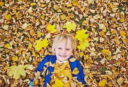 Cheerful boy lying on autumnal ground covered with yellow leaves