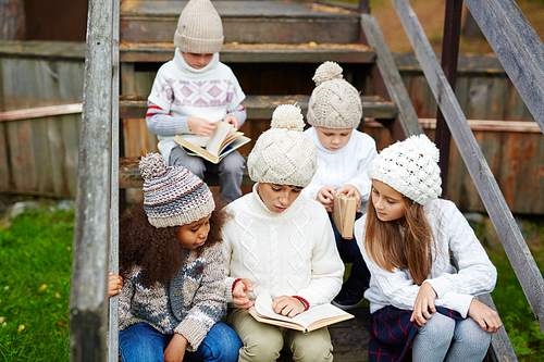 Group of clever kids reading books outdoors