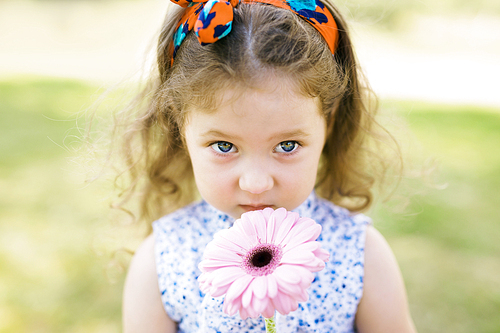 Cute girl smelling pink gerbera outdoors