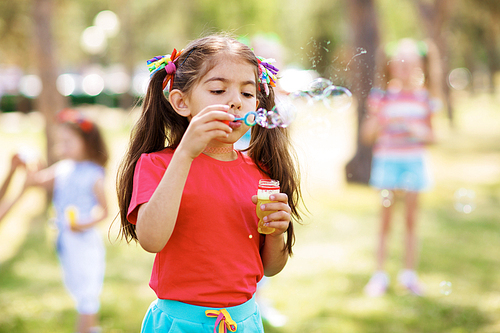 Cute little girl blowing soap bubbles outdoors