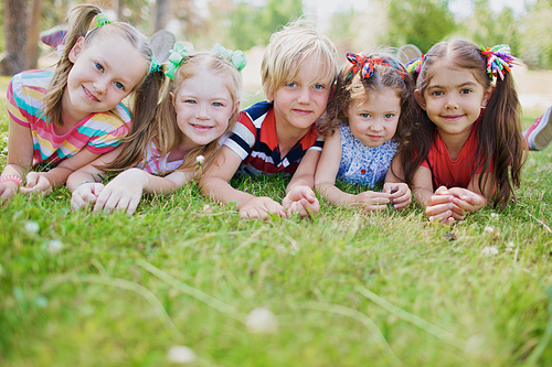 Row of carefree children lying on green grass