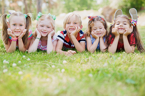 Smiling friends relaxing on green grass on summer day