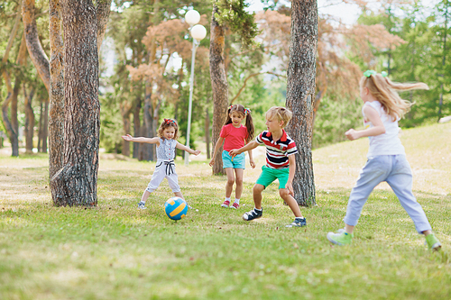 Group of friendly kids playing with ball on green lawn