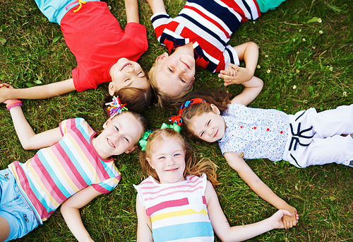 Group of children lying on grass and holding hands