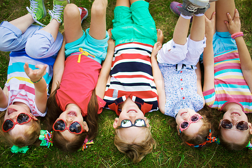 Row of smiling friends in sunglasses lying on grass