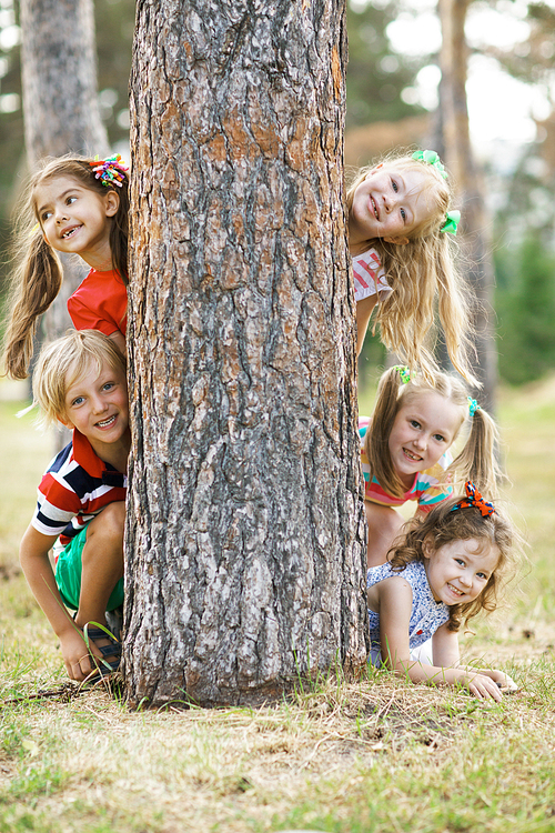 Cute kids peeking out of tree trunk