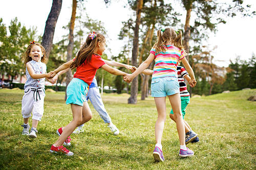 Merry children having round dance on grass