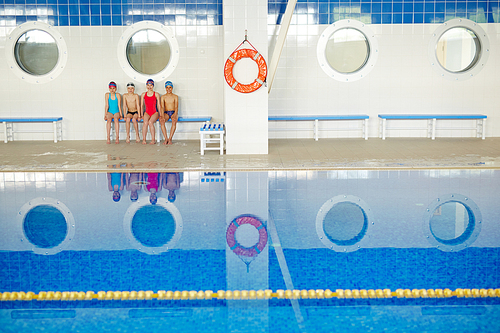 Group of sporty kids sitting on bench by swimming pool