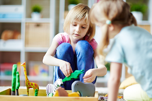 Cute girls playing with toy animals in kindergarten