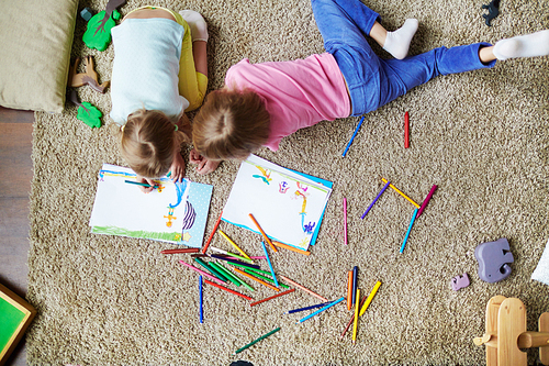 Two girls drawing with highlighters while lying on the floor