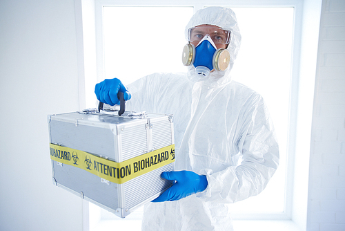 Man in protective overall holding case with biohazard symbol