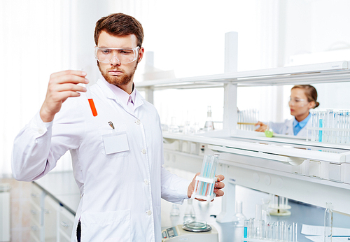 Young chemist looking at fluid substance in flask