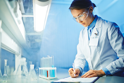 Young laboratory worker making notes upon characteristics of liquids