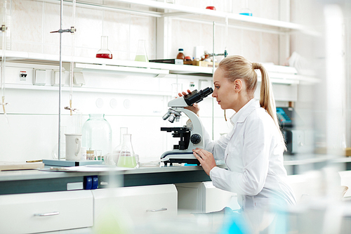Young woman in white-coat studying new virus in microscope