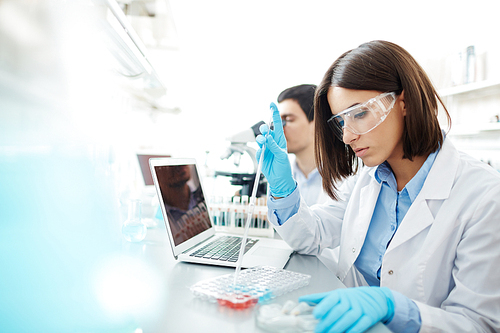 Young woman in whitecoat studying new chemical substances in lab