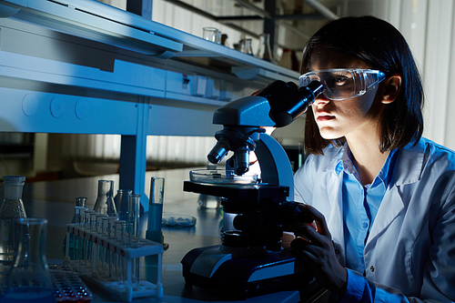 Young specialist looking in microscope during research