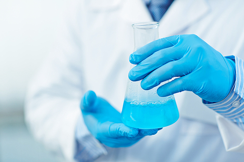 Modern scientist in protective gloves holding tube with blue fluid