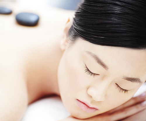 Beautiful Asian woman having stone massage in spa salon