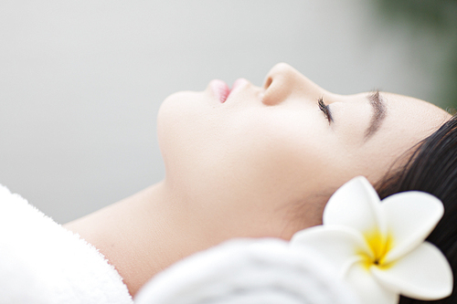 Young Asian woman with frangipani in her hair relaxing in spa salon
