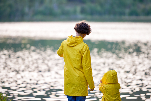 Young woman and her child in yellow raincoats standing in front of river or lake