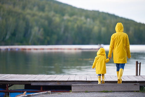 Rear view of woman and child in yellow raincoats and rubberboots walking towards river