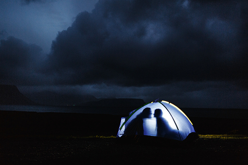 Silhouettes of young lovers in tent among nothern landscape at night